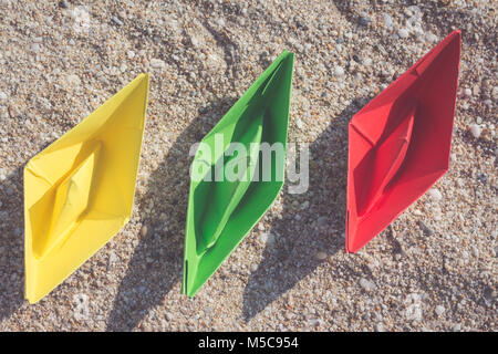 Barche di carta in diversi colori sulla spiaggia sabbiosa. Viaggi e vacanze estive concetti. Foto Stock