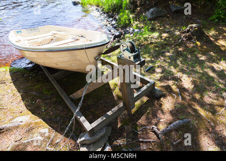 Piccolo bianco in plastica canotto giace sulla costa del lago ancora. Costruzione di argani per tirare le barche a terra Foto Stock