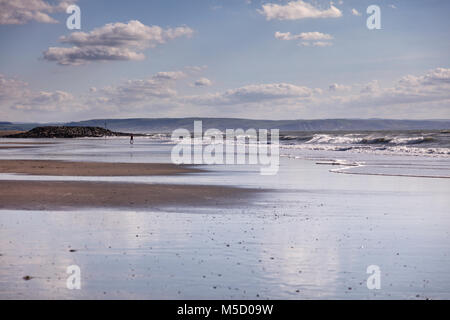 Persona solitaria su una spiaggia deserta a Tywyn nel Galles del Nord su un luminoso ventoso mattina autunnale Foto Stock