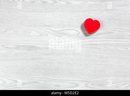 Piccolo rosso a forma di cuore in plastica chiuso casella su un bianco sullo sfondo di legno Foto Stock