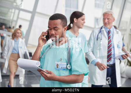 Infermiere con appunti parlando al cellulare nel corridoio di ospedale Foto Stock
