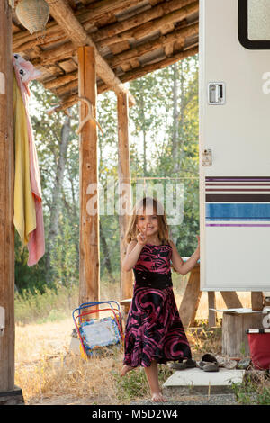 Ritratto sorridente, fiducioso ragazza abito in gesti di pace al di fuori del segno di camper rurale Foto Stock