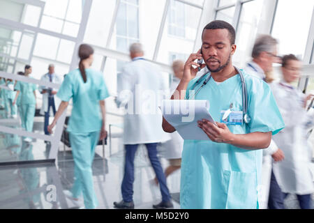 Chirurgo maschio con appunti parlando al cellulare in ospedale lobby Foto Stock