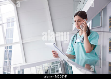 Infermiera femmina con appunti parlando al cellulare in ospedale Foto Stock