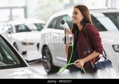 Donna sorridente cliente ibrido portante il cavo per la ricarica in auto lo showroom della concessionaria Foto Stock