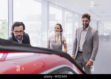 Venditore auto che mostra la nuova vettura per accoppiare i clienti in concessionaria auto showroom Foto Stock