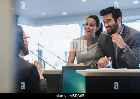 Coppia sorridente i clienti parlando di receptionist al desk in concessionaria auto Foto Stock