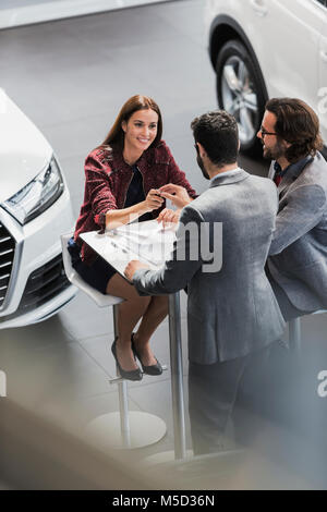 Venditore auto dando le chiavi dell'auto alla femmina sorridente cliente in concessionaria auto showroom Foto Stock