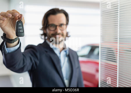 Ritratto fiducioso venditore auto azienda, mostra chiave auto in concessionaria auto showroom Foto Stock