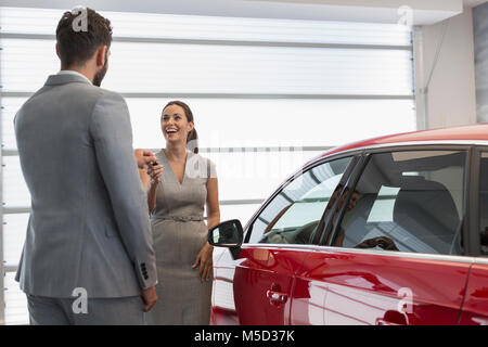 Venditore auto che dà le chiavi a nuove auto per i clienti di sesso femminile in concessionaria auto Foto Stock