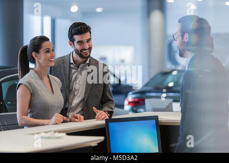 Accoppiare i clienti parlando di receptionist al desk in concessionaria auto showroom Foto Stock