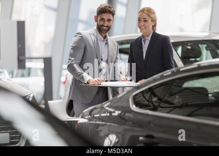 Venditore auto e femminile cercando nuove vetture in concessionaria auto showroom Foto Stock