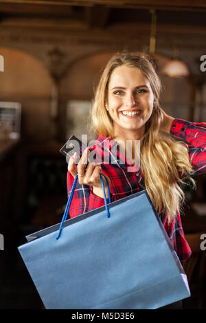 Donna in camicia rossa contiene borsa blu e splendidamente sorrisi Foto Stock