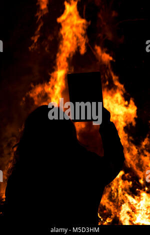 Donna attraente prende un selfie davanti a un grande fuoco durante le ore notturne la festa del villaggio Foto Stock