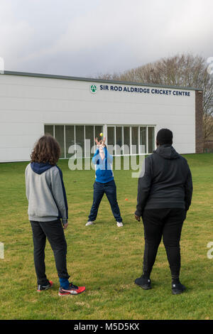 Gli studenti fanno pratica con la riproduzione di cricket su una scuola campo da gioco come parte di una lezione di giochi con il loro insegnante Foto Stock