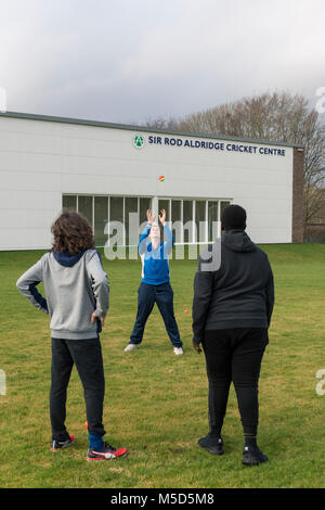 Gli studenti fanno pratica con la riproduzione di cricket su una scuola campo da gioco come parte di una lezione di giochi con il loro insegnante Foto Stock