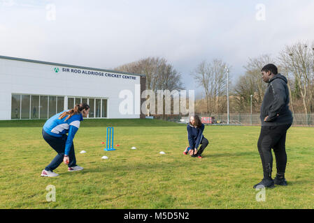 Gli studenti fanno pratica con la riproduzione di cricket su una scuola campo da gioco come parte di una lezione di giochi con il loro insegnante Foto Stock