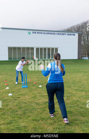 Gli studenti fanno pratica con la riproduzione di cricket su una scuola campo da gioco come parte di una lezione di giochi con il loro insegnante Foto Stock