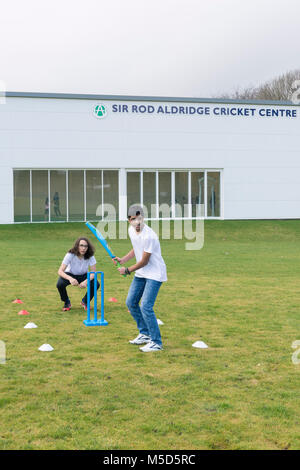 Gli studenti fanno pratica con la riproduzione di cricket su una scuola campo da gioco come parte di una lezione di giochi con il loro insegnante Foto Stock