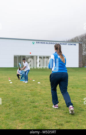 Gli studenti fanno pratica con la riproduzione di cricket su una scuola campo da gioco come parte di una lezione di giochi con il loro insegnante Foto Stock