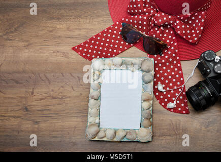 Photo frame realizzato con conchiglie di mare, fotocamera, Red Hat e occhiali da sole, su uno sfondo di legno, foto macro Foto Stock