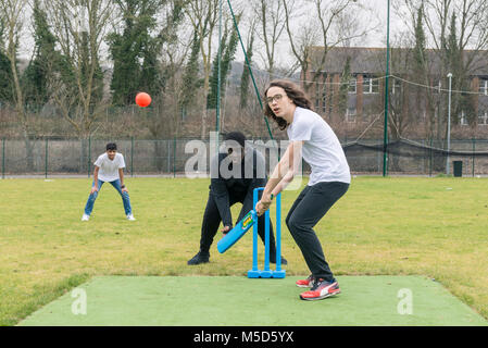 Gli studenti fanno pratica con la riproduzione di cricket su una scuola campo da gioco come parte di una lezione di giochi con il loro insegnante Foto Stock