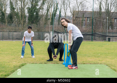 Gli studenti fanno pratica con la riproduzione di cricket su una scuola campo da gioco come parte di una lezione di giochi con il loro insegnante Foto Stock