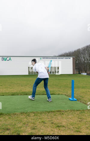 Gli studenti fanno pratica con la riproduzione di cricket su una scuola campo da gioco come parte di una lezione di giochi con il loro insegnante Foto Stock