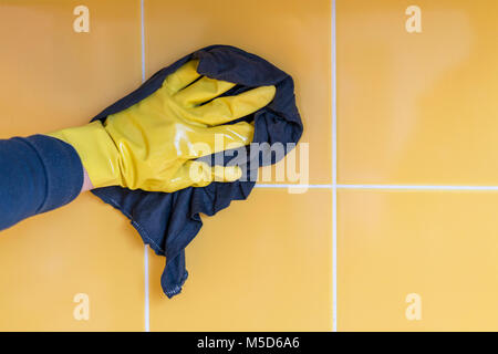La mano in un giallo guanto di gomma lava una parete gialla con un panno Foto Stock