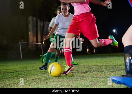 Femmina di giovani calciatori di giocare sul campo di notte, calciare il pallone Foto Stock
