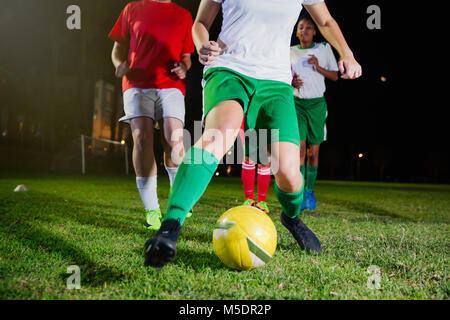 Femmina di giovani calciatori di giocare sul campo di notte, calciare il pallone Foto Stock