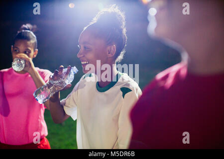 Sorridente giovane femmina i giocatori di calcio in appoggio, bere acqua da bottiglie sul campo di notte Foto Stock