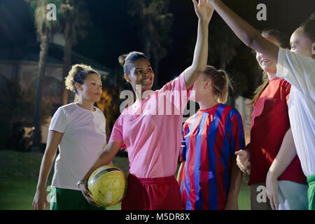 Fiducioso giovane femmina i compagni di squadra di calcio di alta fiving sul campo di notte Foto Stock