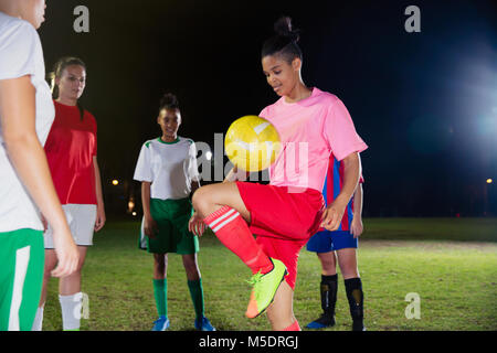 Femmina giovane giocatore di calcio praticanti, la pallina che rimbalza sul ginocchio sul campo di notte Foto Stock