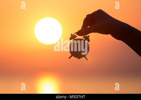 Silhouette di donna mano azienda piccola sveglia e il tramonto sul mare in background. Alzarsi presto concetto. Foto Stock