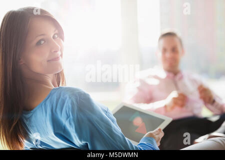 Ritratto di giovane e bella imprenditrice azienda tavoletta digitale con il collega di sesso maschile in background in ufficio Foto Stock