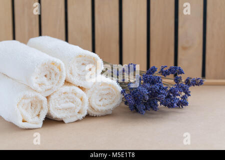 Il beige asciugamani da bagno su sfondo di legno e un mazzetto di lavanda essiccata. Spa concept Foto Stock