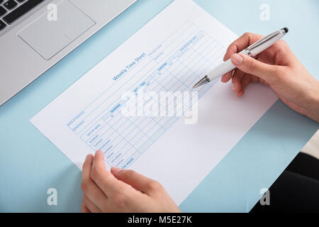 Close-up di una imprenditrice di riempimento del tempo settimanale foglio sulla scrivania blu Foto Stock