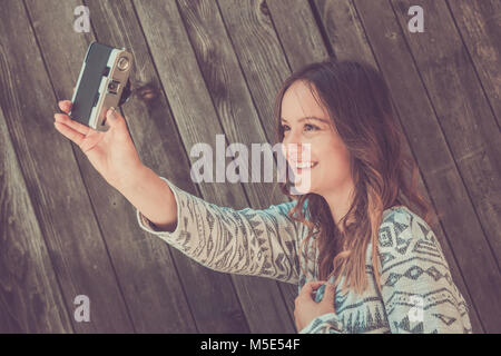 Ritratto di giovane bellissima femmina tenendo autoritratto usando retro vintage fotocamera a pellicola contro lo sfondo di legno Foto Stock