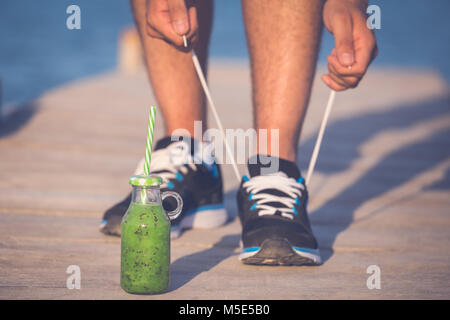 Frullato verde fitness allacciatura uomo scarpe da corsa. Atleta runner con verdura verde succo detox ottenere pronto per la corsa mattutina in esecuzione di legatura laccio Foto Stock