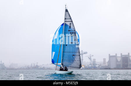 Un 22 Metri di yacht in legno flying blue spinnaker vele passato il paesaggio industriale di Plymouth è Devonport Dockyard. Foto Stock