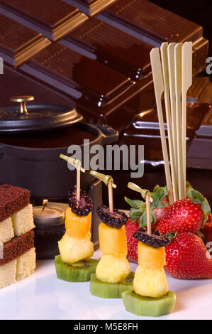 Gigantesco barrette di cioccolato fondente dietro assortimento di frutta, fragole, Mango, ananas, lampone, kiwi e pezzi di torta come dessert di immersione. Foto Stock