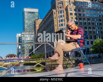 Rilassata coppia lavoratori autonomi imprenditore esterno sul suo ufficio barca parlando su iPhone funziona lo smartphone a un computer portatile Canary Wharf London E14 Foto Stock