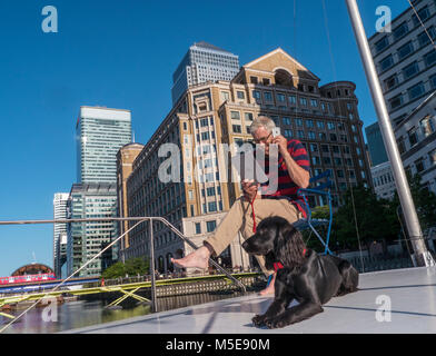 Uomo maturo city location & spaniel cane fuori su office barge boat parlando su smartphone iPhone & iPad controllo computer Canary Wharf London E14 Foto Stock