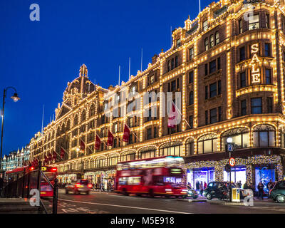 Harrods vendita luci crepuscolo grande magazzino illuminato di notte con 'Salo' segno shopping acquirenti autobus rossi e passando taxi sulla ULEZ Route Knightsbridge Londra SW1 Foto Stock