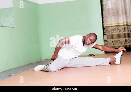 Giovane uomo gambe divaricate seduti su un tappeto stretching in palestra. Coscia fortificare il movimento. Foto Stock