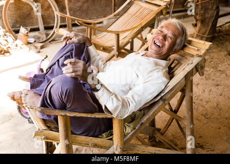 Bagan, Myanmar, Dicembre 27, 2017: Senior l uomo recupera in una poltrona e fuma una sigaretta Foto Stock