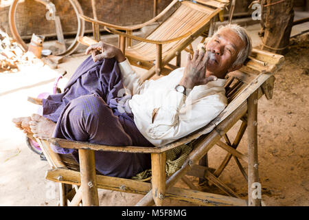 Bagan, Myanmar, Dicembre 27, 2017: Senior l uomo recupera in una poltrona e fuma una sigaretta Foto Stock