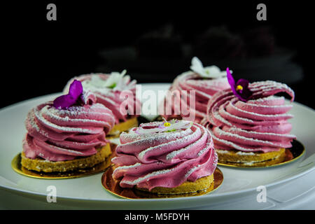 Rosa zephyr cookies decorati con fiori viola sulla piastra bianca con sfondo nero Foto Stock