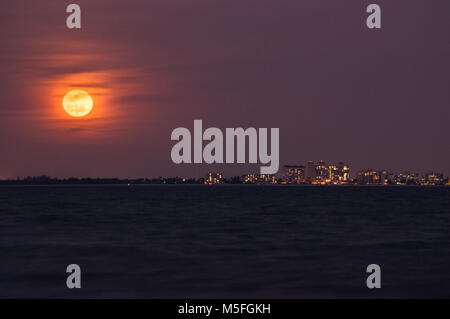 Una piena luna rossa sorge sopra i grandi appartamenti che la linea dell'orizzonte di bordo attraverso la spiaggia di Fort Myers in Florida.